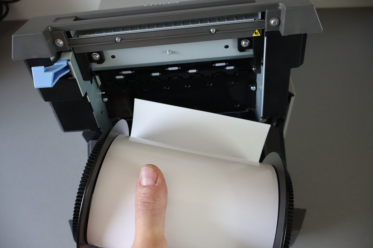 Neue Papierrolle wird in den Drucker eingesetzt, Papier wird unter die Führungsrollen geführt