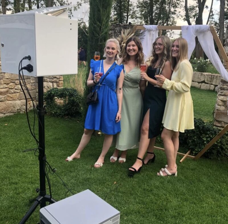 Freundinnen in bunten Kleidern posieren vor der SmileCube Fotobox auf einer Outdoor-Hochzeit