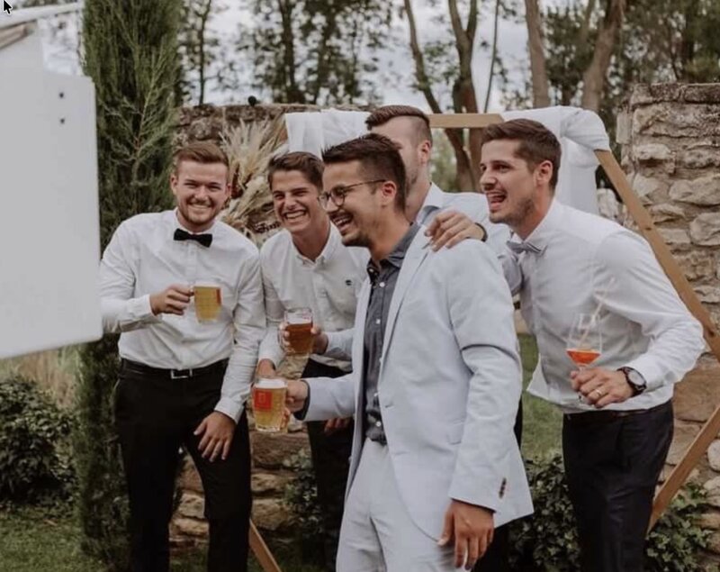 Lachende Hochzeitsgäste mit Drinks vor der SmileCube Fotobox im Garten